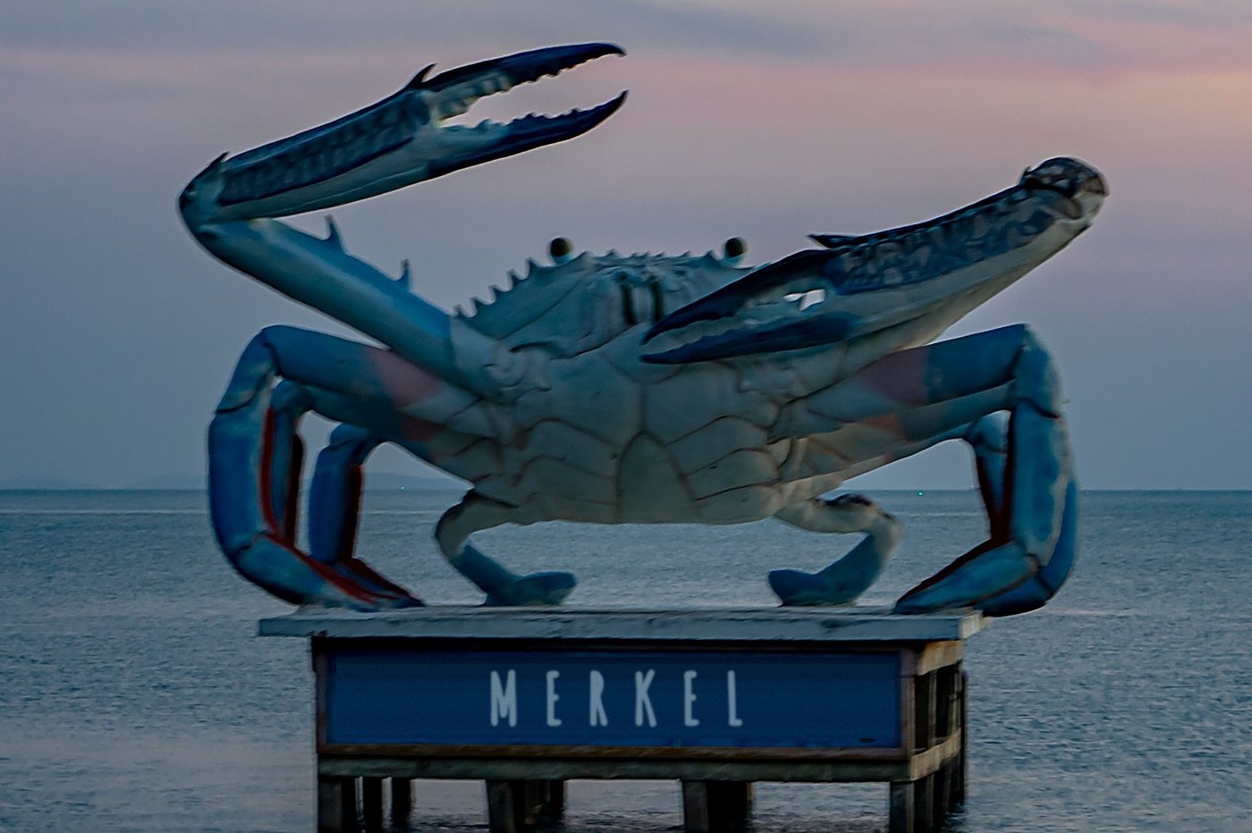 A giant blue crab statue on a platform in the sea at dusk